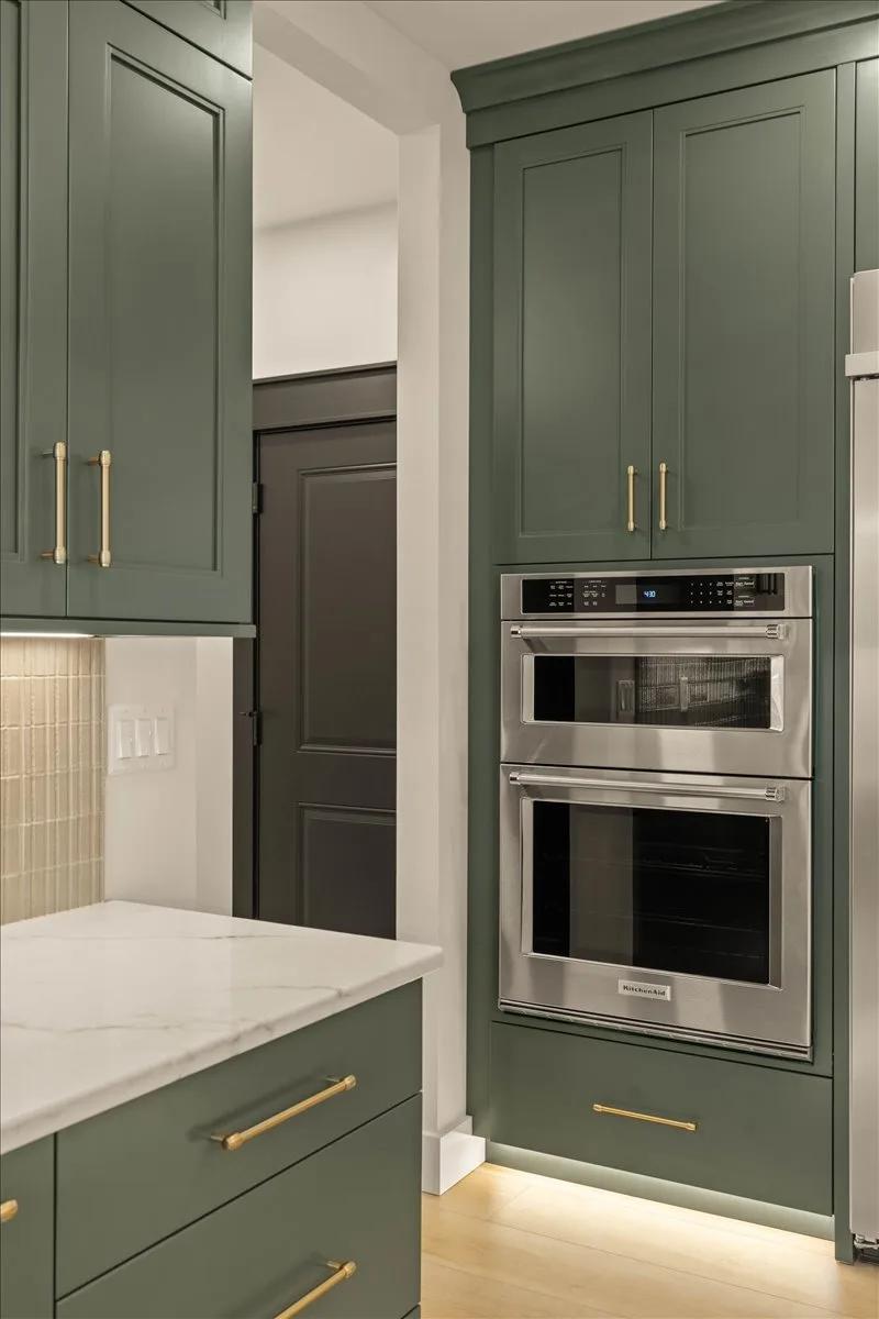 Shade Grown American Collection cabinets with built-in wall ovens, gold hardware, and a stacked tile backsplash