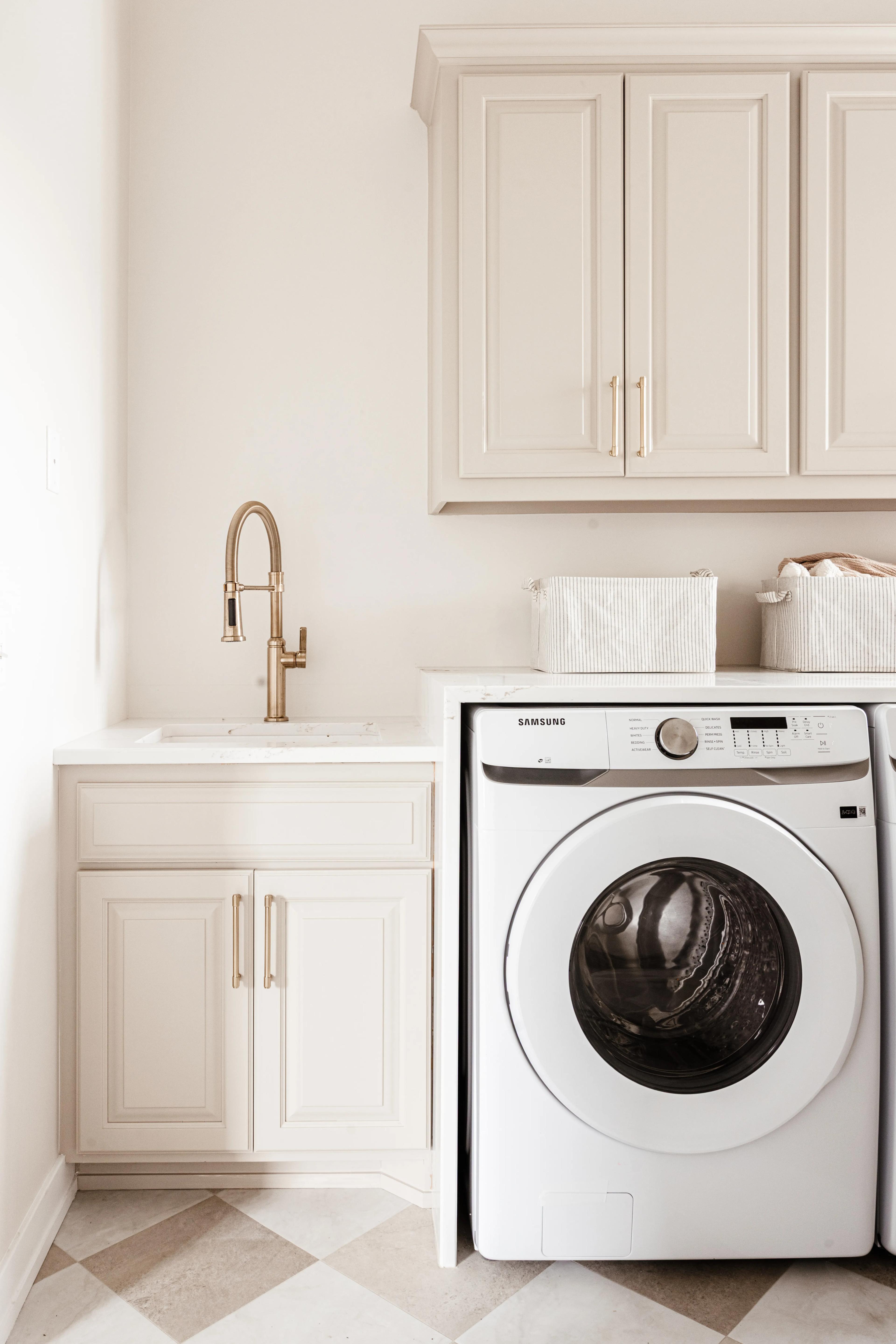 Laundry cabinets in Accessible Beige Plateau with gold hardware and a sink beside a washer